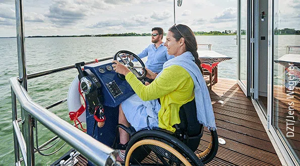 eine Frau im Rollstuhl steuert ein Febomobil, dahinter sitzt ein junger Mann
