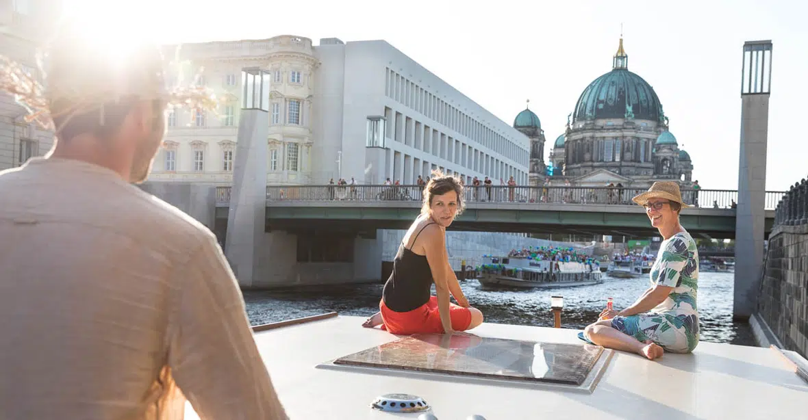 eine Kormoran fährt durch Berlin, an Deck 2 Frauen, im Hintergrund der Berliner Dom