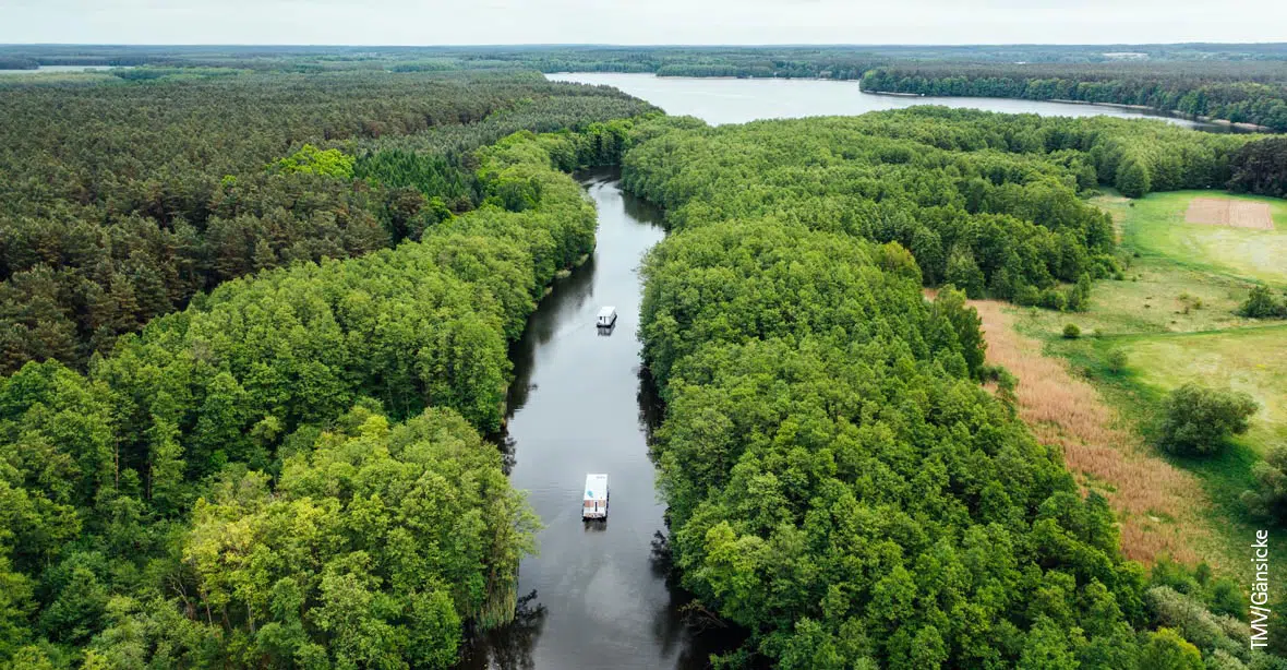 Luftaufnahme auf eine Wasserlandschaft mit einem Fluss, auf dem 2 Boote fahren